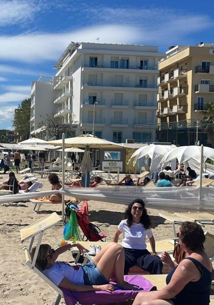 Spiaggia affollata con lettini e ombrelloni, edifici sullo sfondo.