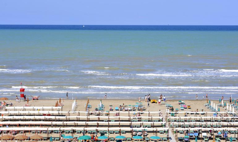 Spiaggia affollata con ombrelloni e mare calmo.