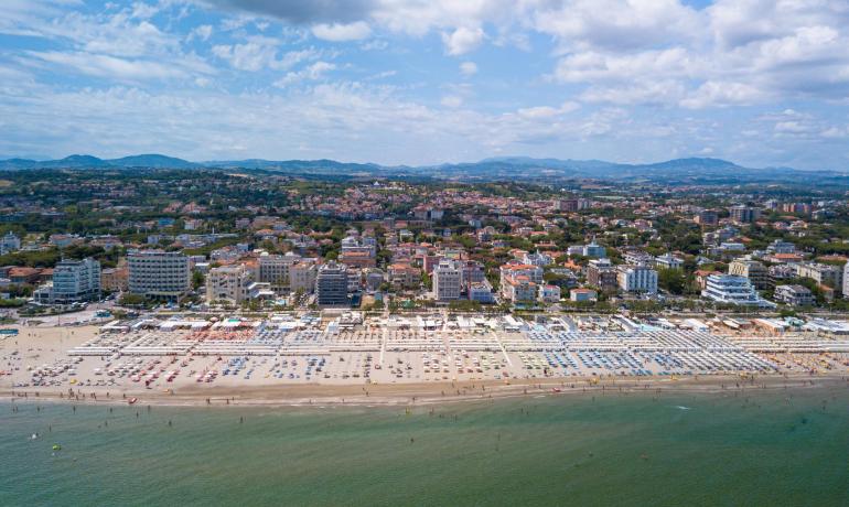 Vista aerea di una spiaggia affollata con ombrelloni colorati e città sullo sfondo.