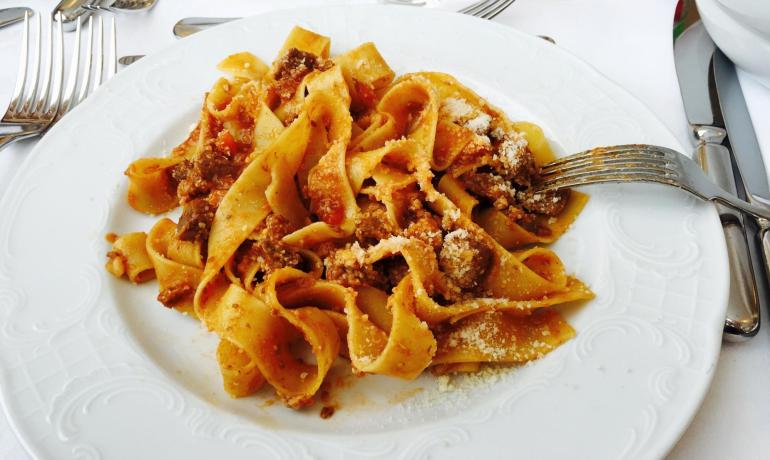 Pappardelle al ragù con parmigiano su piatto bianco.