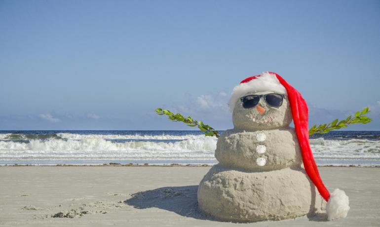 Pupazzo di sabbia con cappello di Natale e occhiali da sole sulla spiaggia.