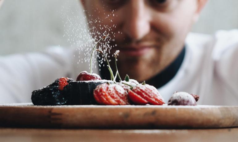 Chef spolvera zucchero a velo su dessert con fragole.