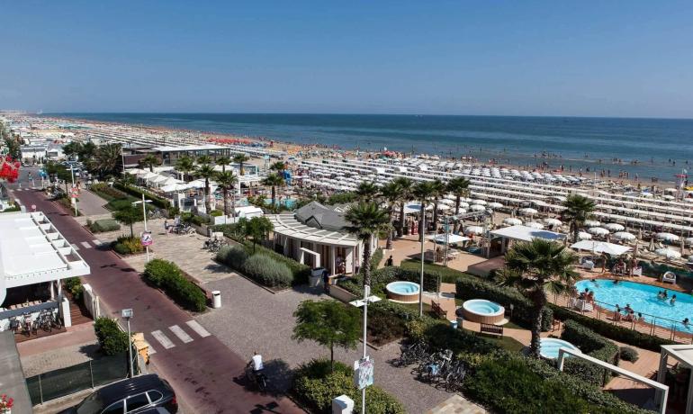 Spiaggia affollata, ombrelloni bianchi, mare blu, giornata estiva vivace e soleggiata.