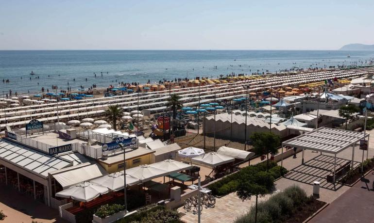 Spiaggia affollata con ombrelloni colorati e mare calmo.