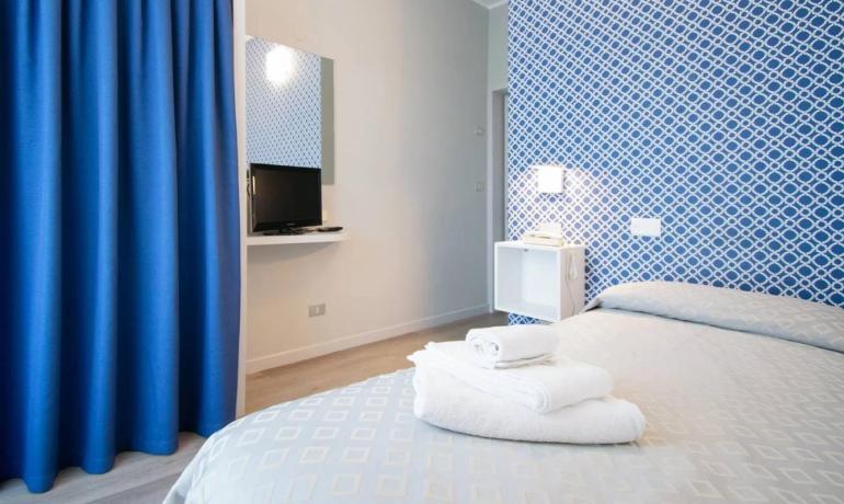 Camera moderna con pareti blu e TV, letto con asciugamani.