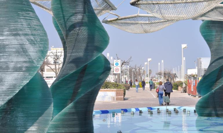 Scultura moderna in vetro su lungomare con passanti.