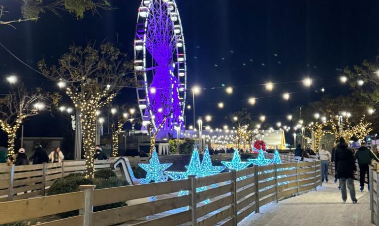 Pista di pattinaggio con ruota panoramica e luci scintillanti.
