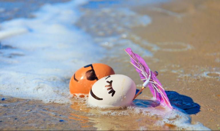 Uova sorridenti sulla spiaggia con ombrellino rosa.