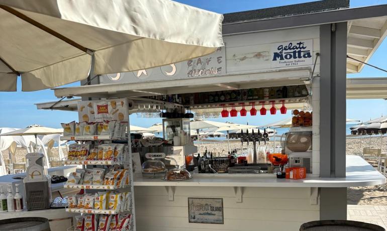 Chiosco sulla spiaggia, sole splendente, atmosfera rilassata e profumo di mare.