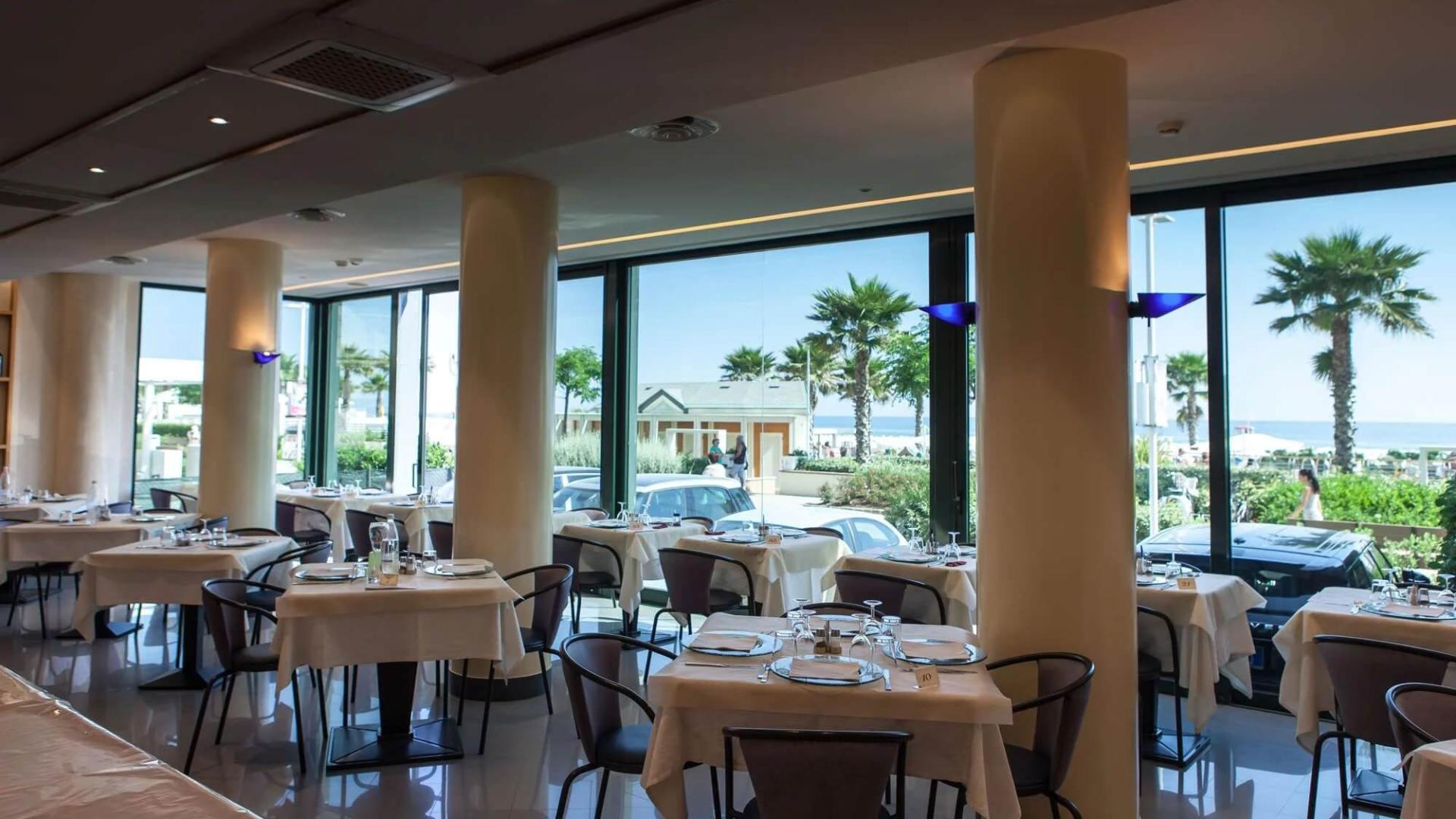 Ristorante elegante con vista mare, tavoli apparecchiati e ampie finestre panoramiche.