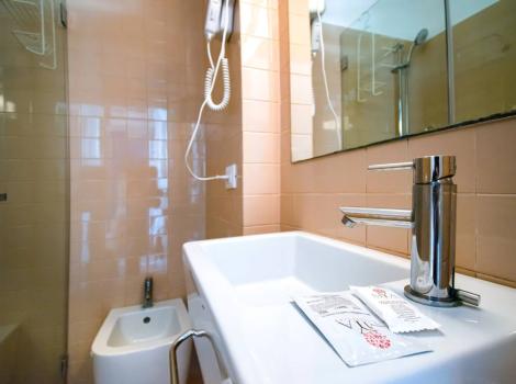 Bagno moderno con lavabo, bidet, specchio e asciugacapelli appeso al muro.