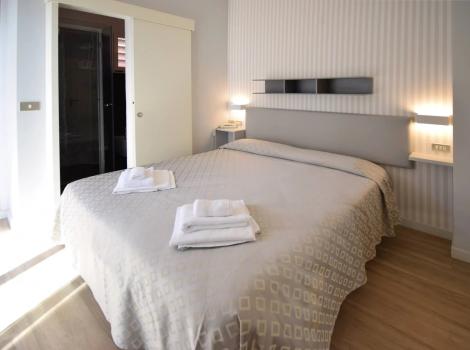 Camera moderna con letto matrimoniale, asciugamani piegati, luci soffuse e porta scorrevole.