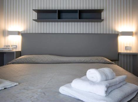 Camera moderna con letto matrimoniale, luci soffuse e asciugamani bianchi piegati.