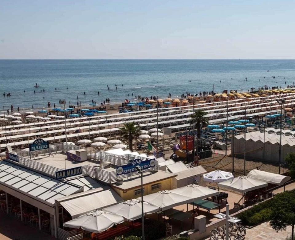 Spiaggia affollata con ombrelloni, palme e strutture balneari sul lungomare.