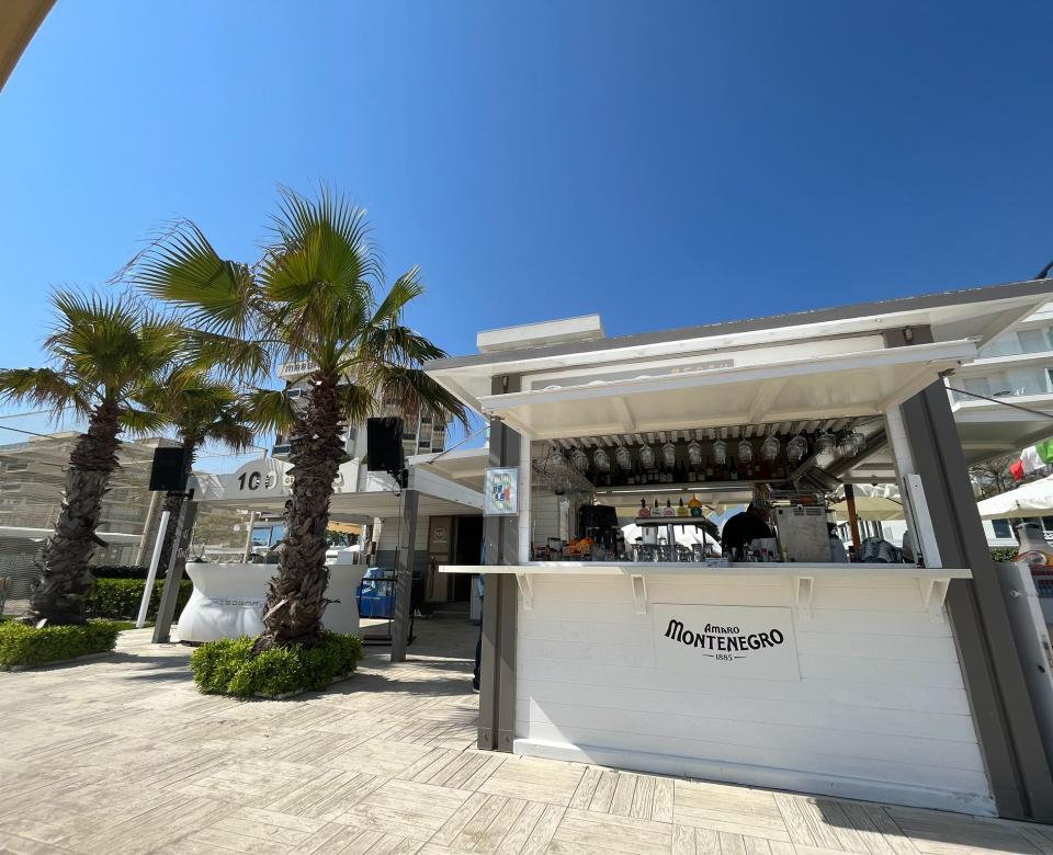 Spiaggia affollata con ombrelloni, palme e strutture vicino al mare.